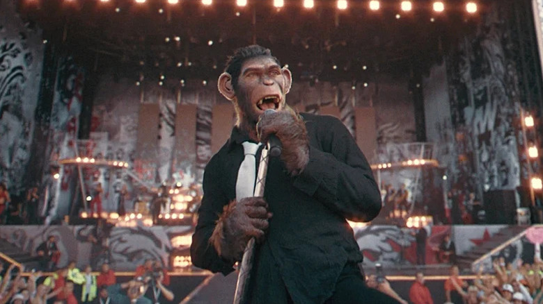 CGI chimpanzee in black shirt and white tie singing on stage in Better Man