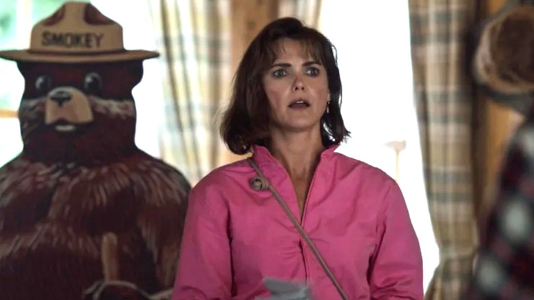 Keri Russell as Sari wearing pink jumpsuit standing in front of Smokey the Bear cutout in Cocaine Bear