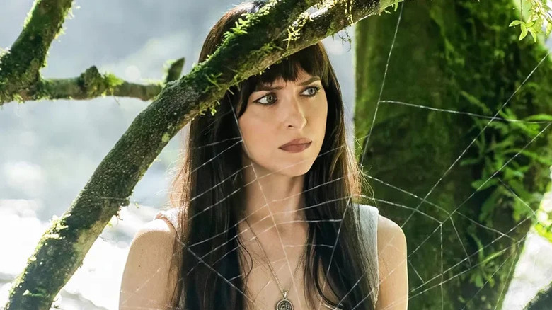 Dakota Johnson as Cassandra Webb standing by tree with spider web in front of her in Madame Web