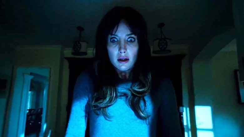 Annabelle Wallis as Madison in dark room looking down at something in horror in Malignant