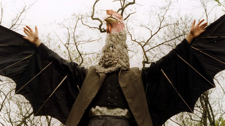 Petr Meissel, with only hands visible, wearing chicken head and wings in Conspirators of Pleasure