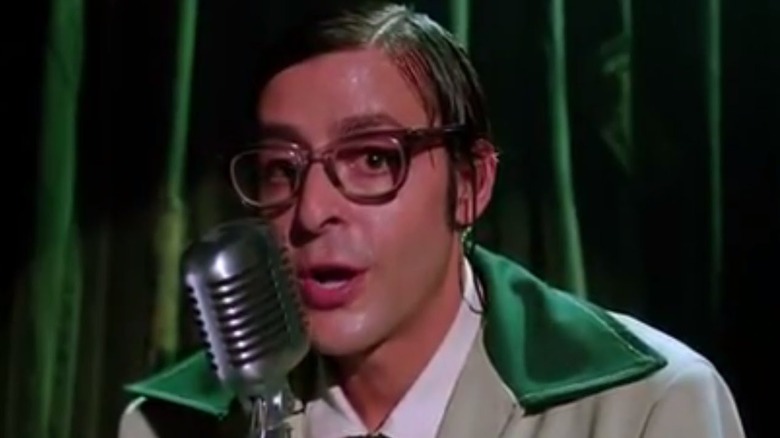 Judd Nelson with greasy hair, glasses, and a green jacket as Marty Malt in The Dark Backward