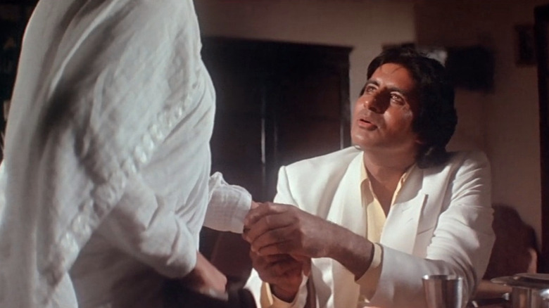 Amitabh Bachchan as Vijay wearing white and looking up at his mother Suhasini (Rohini Hattangadi) and holding her hand in Agneepath (1990)
