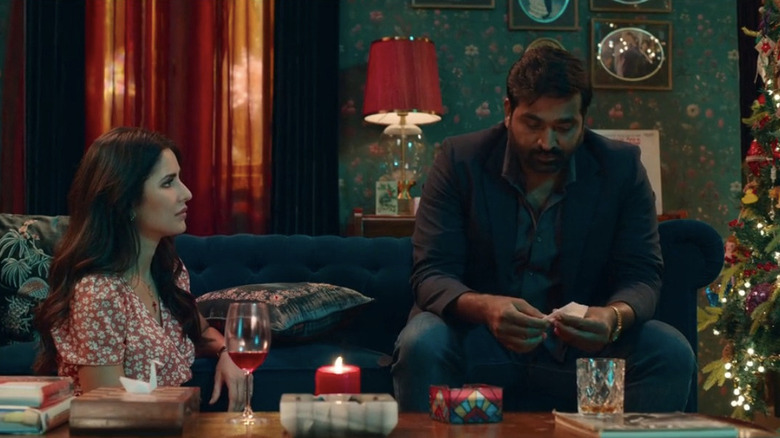Katrina Kaif as Maria sitting on floor in floral dress next to Vijay Sethupathi as Albert sitting on couch in Merry Christmas