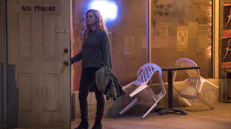 Camille Preaker (Amy Adams) holds open a door to a dingy bar that has "no minors" written on it in Sharp Objects