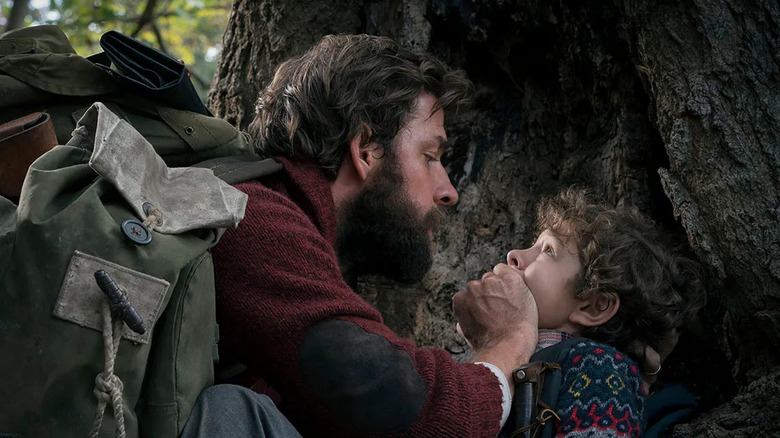 John Krasinski and Noah Jupe as Lee and Marcus, hiding behind a tree in A Quiet Place