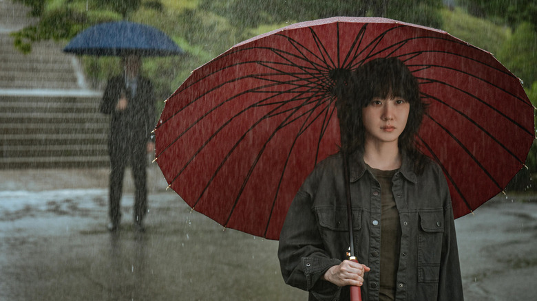 Jung Se-ok (Park Eun-bin) stands under an umbrella in heavy rain as a man watches in Hyper Knife