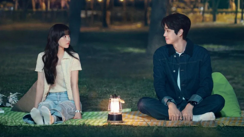 Kim Mu-bee (Park Bo-young) and Ko Gyeom (Choi Woo-sik) sit on blanket in a park at night with a lit lantern between them in Melo Movie