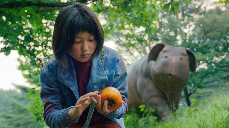 Mija (Ahn Seo-hyun) examines a persimmon as Okja watches in Okja