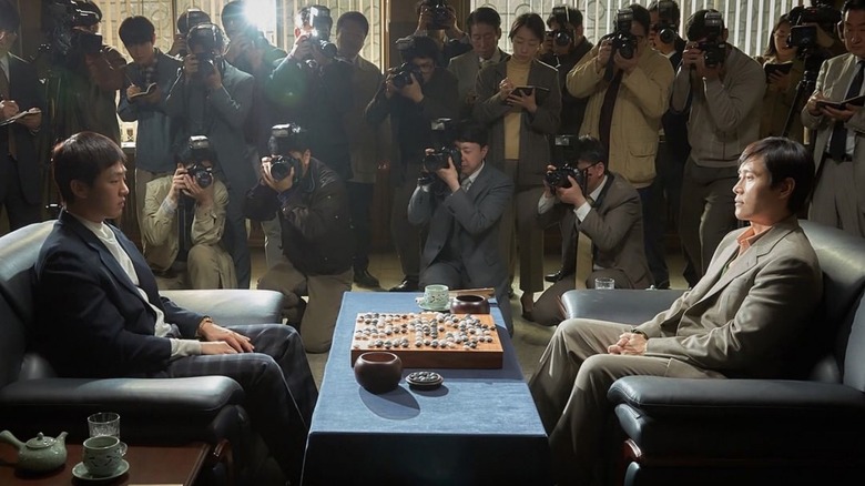 Photographers take pictures of Lee Chang-ho (Yoo Ah-in) and Cho Hun-hyun (Lee Byung-hyun) as they face each other over a Go board in The Match