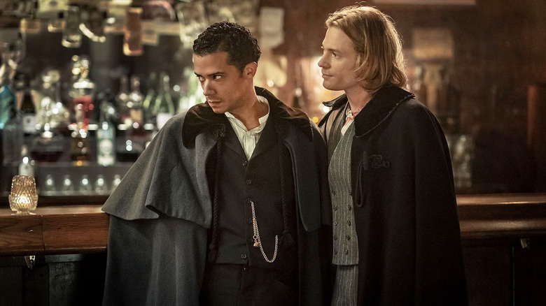 Sam Ried as Lestast and Jacob Anderson as Louis wearing fancy clothes and cloaks in a bar in Interview With a Vampire