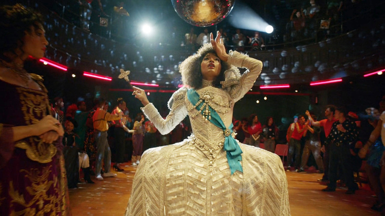 Indya Moore as Angel wearing white Victorian ball gown beneath disco ball and surrounded by people in Pose