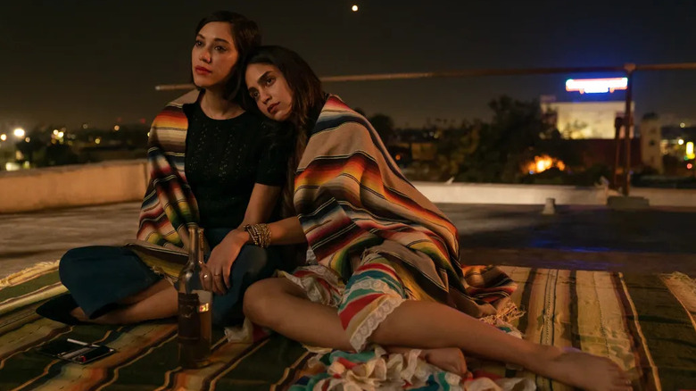 Mishel Prada as Emma and Melissa Barrera as Lyn sitting on a blanket on the rooftop in Vida