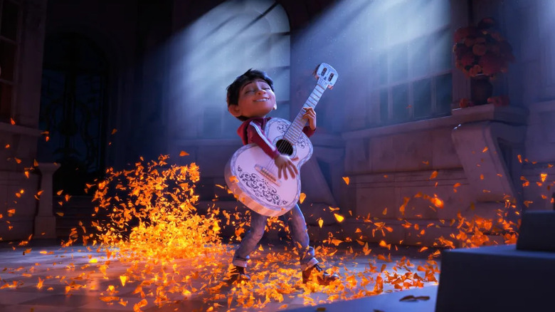 Miguel (Anthony Gonzalez) plays a guitar as glowing leaves blow around him in Coco