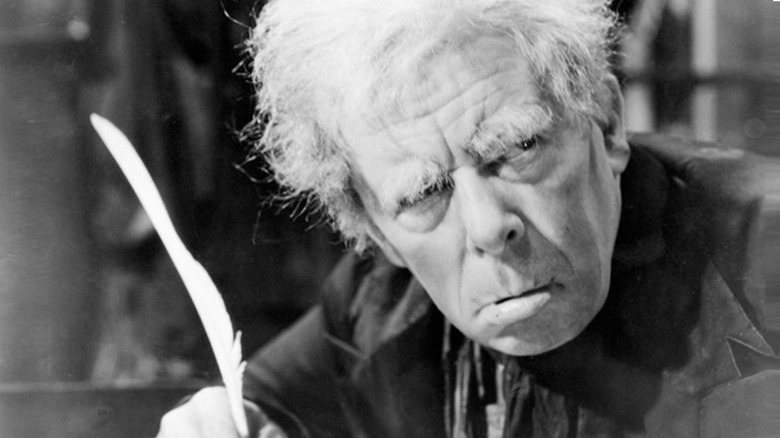 Ebenezer Scrooge (Seymour Hicks) looks up glaring while writing with a quill in Scrooge (1935)