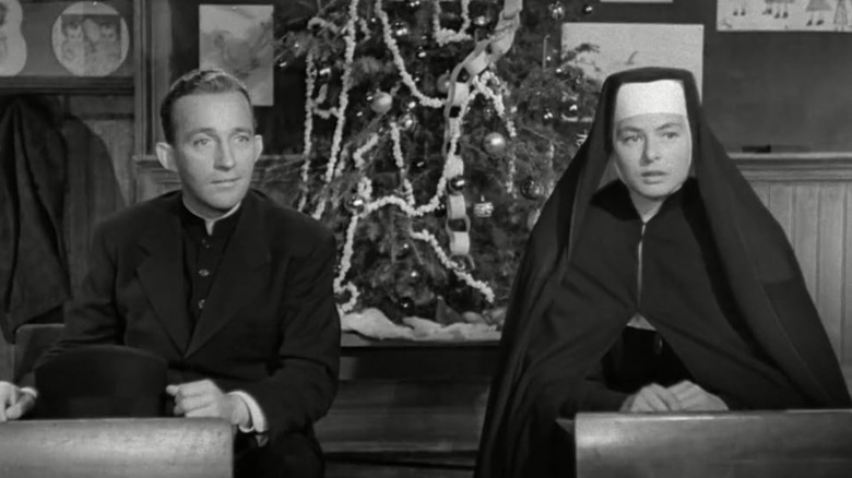 Father Chuck O'Malley (Bing Crosby) and Sister Mary Benedict (Ingrid Bergman) sit at desks in front of a Christmas tree in The Bells of St. Mary's