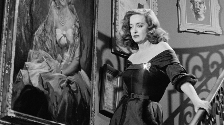 Bette Davis as Margot Channing standing on the stairs in All About Eve