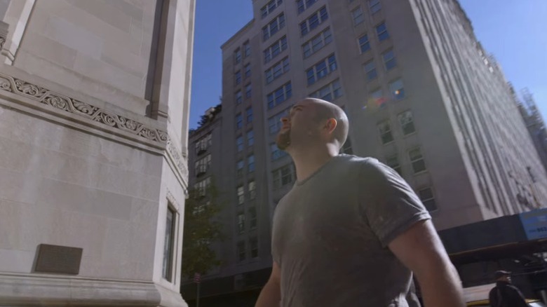 Sasha Neulinger looking up while walking between tall buildings in Rewind
