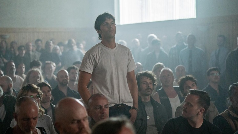 Nicholas Hoult as Bob Mathews stands in a seated crowd in The Order.