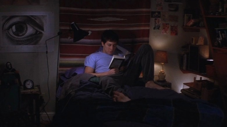 Jake Gyllenhaal as Donnie Darko sitting on his bed and reading a book in Donnie Darko