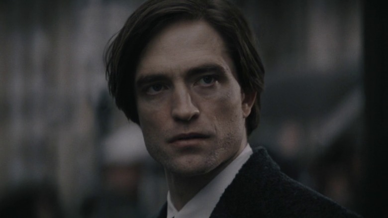 Robert Pattinson as Bruce Wayne standing out in the street with a stern expression in The Batman