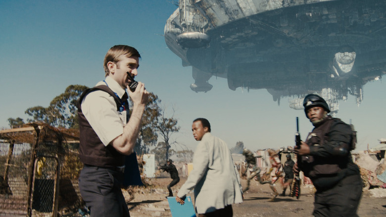 Wikus (Sharlto Copley) speaks on a radio while walking by a hovering spaceship in District 9
