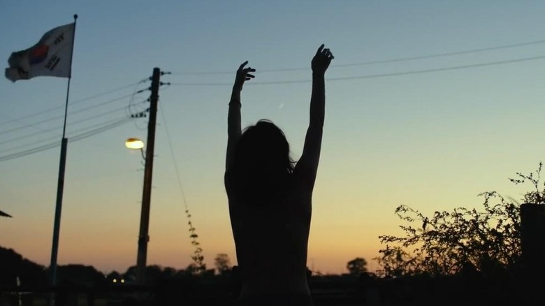 Jeon Jong-seo as Shin Hae-mi in Burning, dancing with her arms up as a silhouette against the sky.