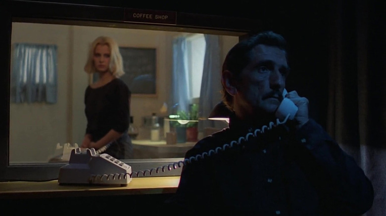 Harry Dean Stanton as Travis Henderson and Nastassja Kinski as Jane Henderson in Paris, Texas, as Travis holds a landline phone to his hear, his back to Jane as she looks at him from the opposite side of a window.