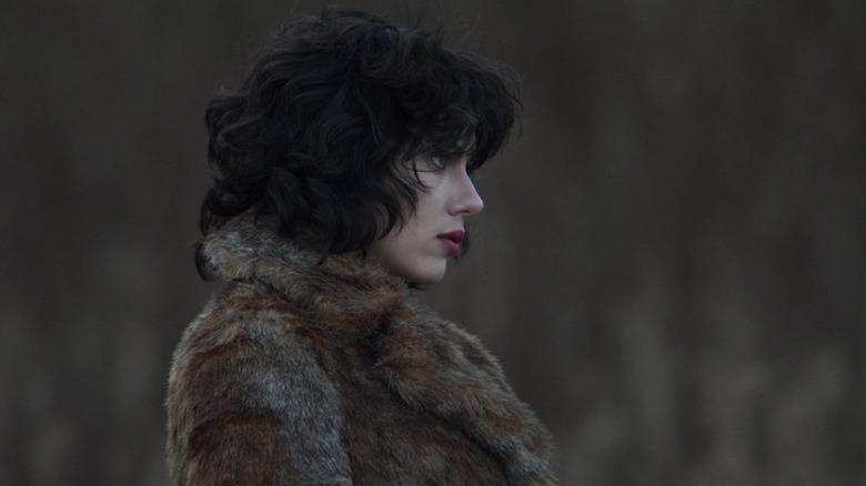 A side profile of Scarlett Johansson as The Female in Under The Skin, wearing a fur coat and looking ominously towards something out of frame.