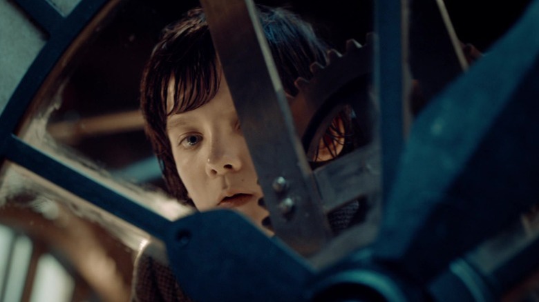 Asa Butterfield as Hugo Cabret looking through the spokes of a wheel in Hugo
