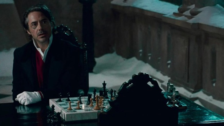 Robert Downey Jr. as Sherlock Holmes sitting at a chess table and talking to a standing Jared Harris as James Moriarty in Sherlock Holmes: A Game of Shadows