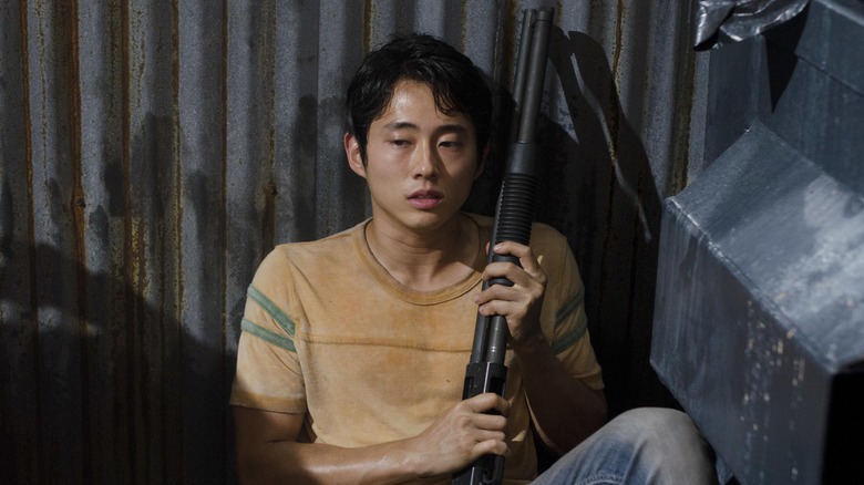 Glenn (Steven Yeun) holds a shotgun, concerned, in The Walking Dead