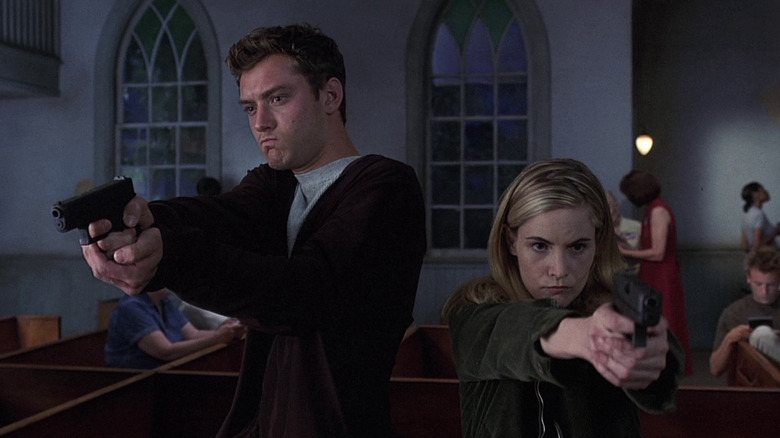 Jude Law as Ted Pikul and Jennifer Jason Leigh as Allegra Geller in eXistenZ, both armed and pointing their guns.