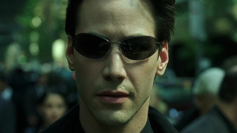 Keanu Reeves as Neo in The Matrix, wearing his oblong shades and centered, looking towards the camera
