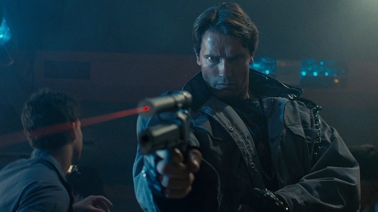Arnold Schwarzenegger as The Terminator in The Terminator, his gun with a laser sight drawn and pointed out past toward the camera.