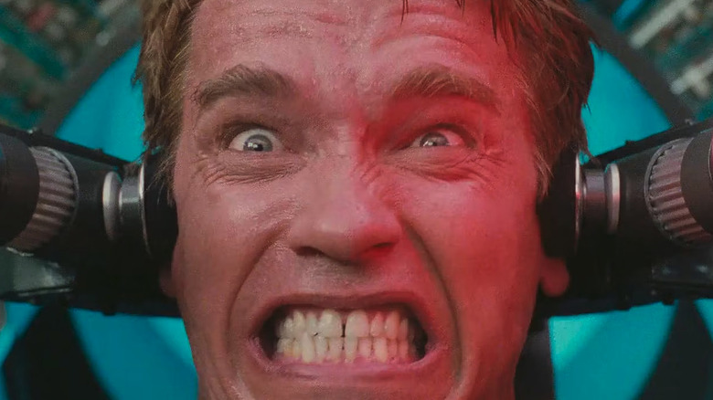 Arnold Schwarzenegger as Douglas Quaid / Carl Hauser in Total Recall, hiding behind a structure and brandishing a weapon.