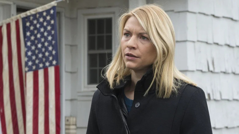 Claire Danes as Carrie Mathison wearing black coat standing in front of white house with American flag hanging out front in Homeland