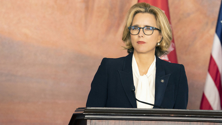 Téa Leoni as President Elizabeth McCord with blue blazer and glasses standing in front of podium with American flag behind her