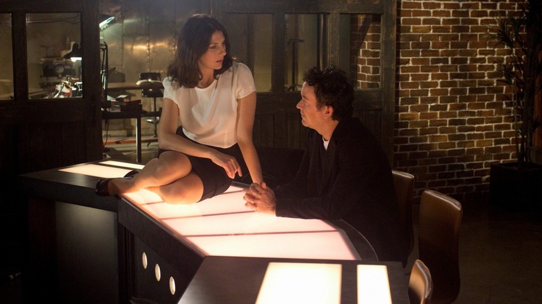 Sophie Devereaux (Gina Bellman) sits on a lit table by Nate Ford (Timothy Hutton) on Leverage