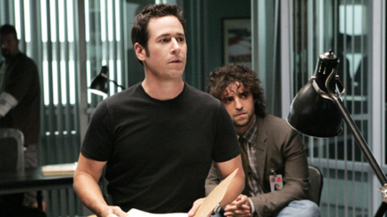Don Eppes (Rob Morrow) opens a file while Charlie Eppes (David Krumholtz) sits on a desk on Numbers