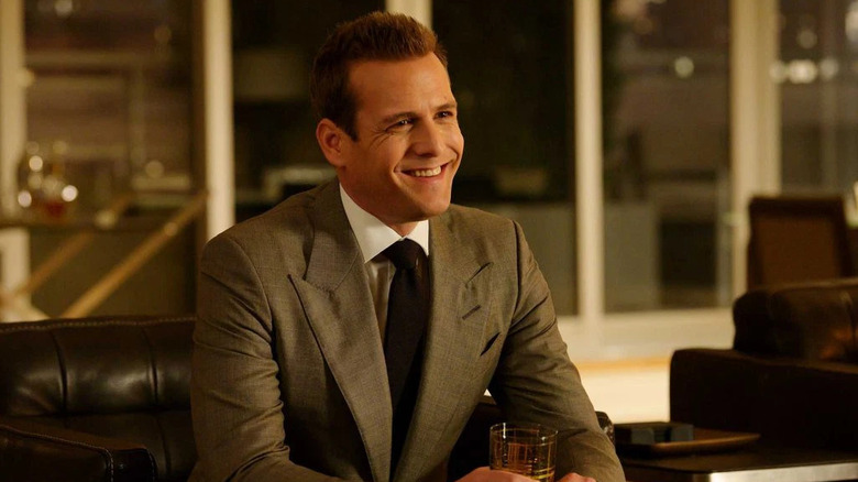 A smiling Harvey Specter (Gabriel Macht) sits holding a drink in Suits