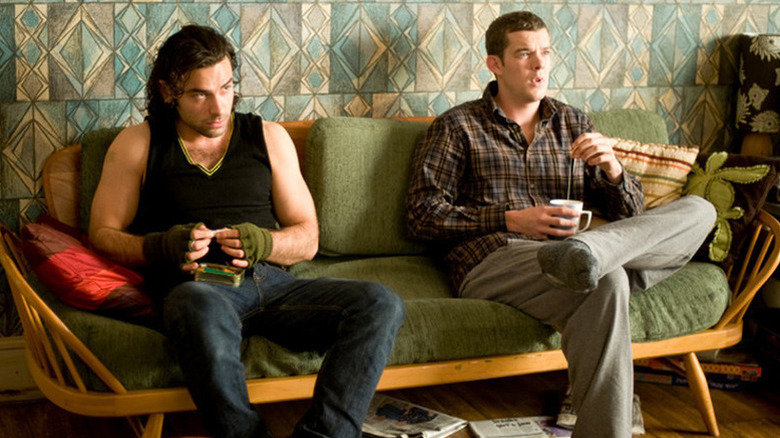 Aidan Turner as John Mitchell sitting on the couch rolling a cigarette next to Russell Tovey as George Sands holding a cup of tea in the UK version of Being Human