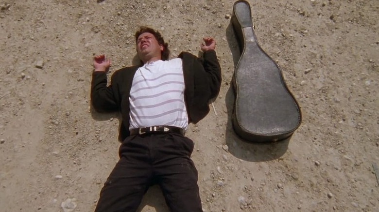 El Mariachi (Carlos Gallardo) lies in the dirt next to his guitar case in El Mariachi