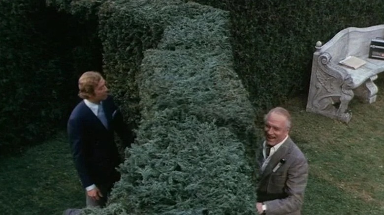 Michael Caine as Milo Tindle and Laurence Olivier as Andrew Wyke standing on opposite sides of a hedge in Sleuth