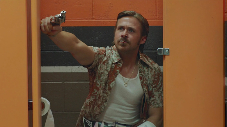 Holland March (Ryan Gosling) sitting inside a toilet stall with a pistol in The Nice Guys (2016).