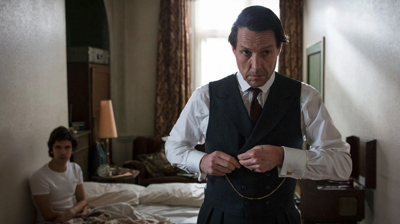 Jeremy Thorpe (Hugh Grant) getting dressed in a bedroom while Norman Scott (Ben Whishaw) sits in bed behind him in A Very English Scandal