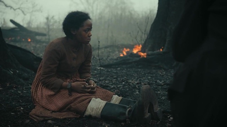 Cora (Thuso Mbedu) sitting in burnt forest in The Underground Railroad