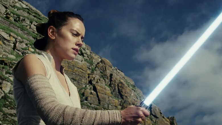 Daisy Ridley as Rey, holding Luke's lightsaber in Star Wars: The Last Jedi.