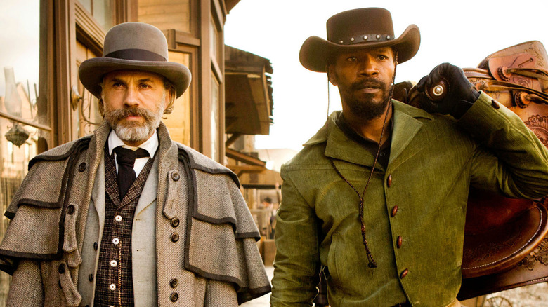 Hannibal Schultz (Christoph Waltz) and Django (Jamie Foxx) walk down a frontier town street, with Django carrying a saddle in Django Unchained
