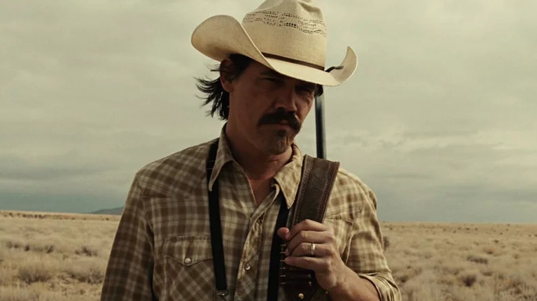 Llewelyn Moss (Josh Brolin) stands on the prairie with a rifle over his shoulder in No Country for Old Men
